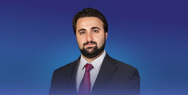 A portrait-style image of an individual in formal business attire positioned against a smooth blue gradient background.