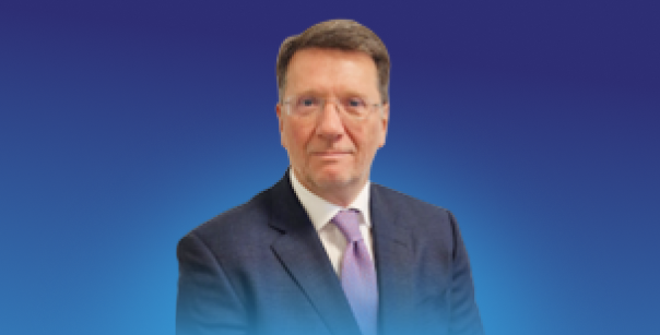 A portrait-style image of an individual in business attire positioned against a blue gradient background.