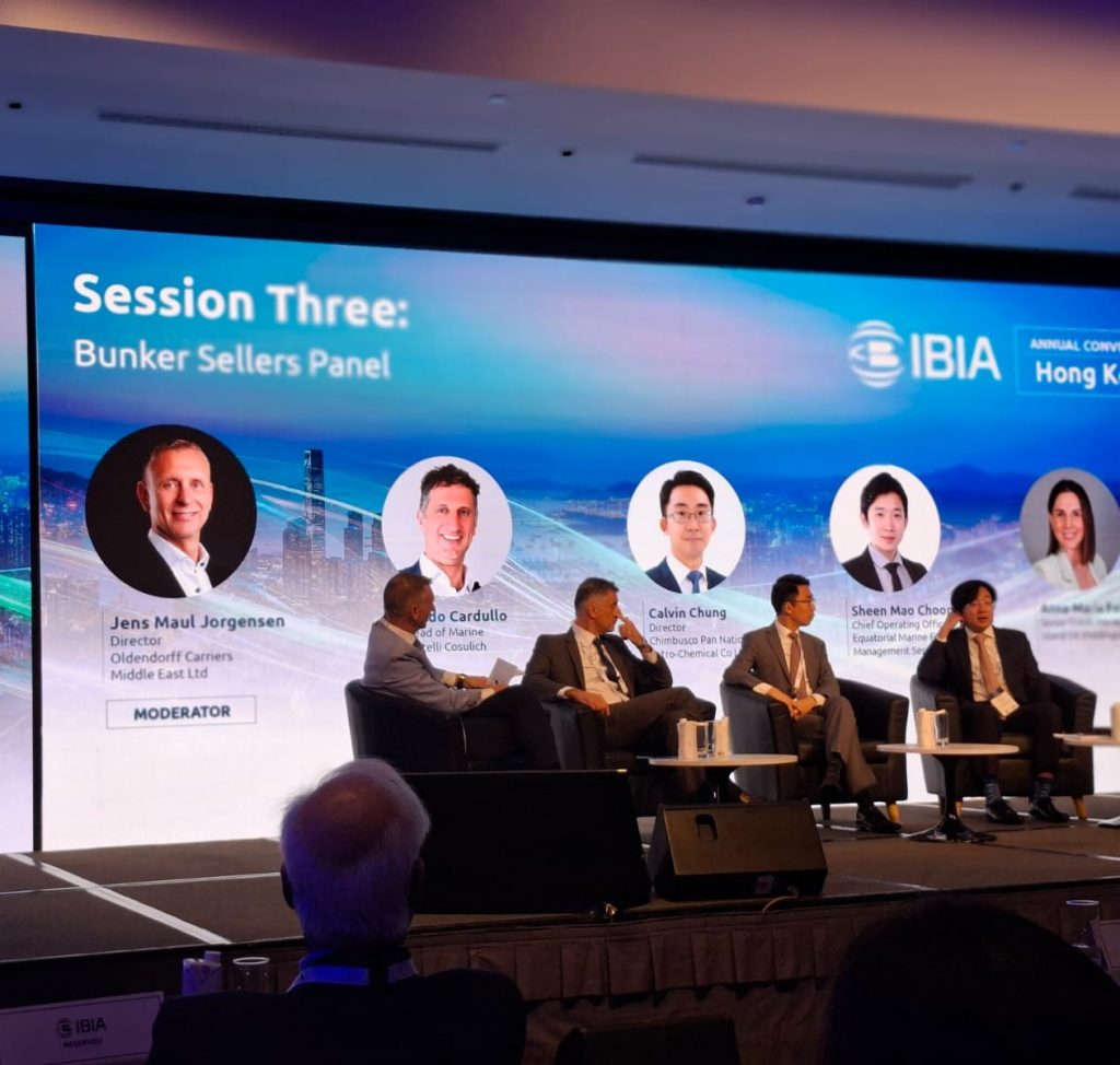 A conference panel session on a stage with multiple speakers seated in front of a large screen that reads “Session Three: Bunker Sellers Panel.”