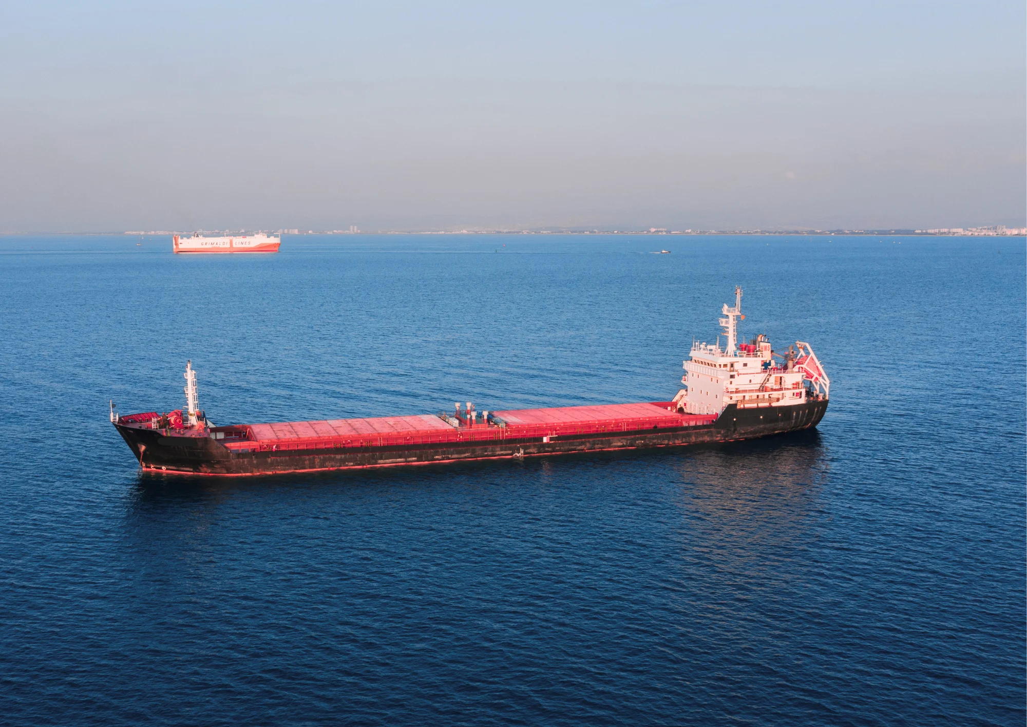 A large cargo ship sailing on open blue water with another vessel visible in the distance.
