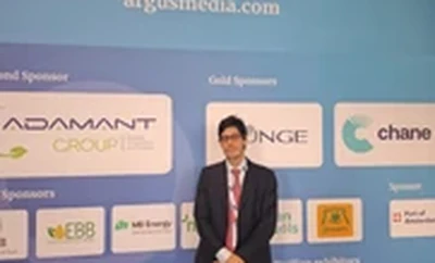 A person standing in front of a blue event backdrop featuring sponsor logos including Adamant Group, Change, EBB, and others at a conference.