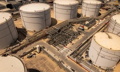 An aerial view of a large industrial facility with multiple cylindrical storage tanks connected by pipelines and surrounded by service roads.