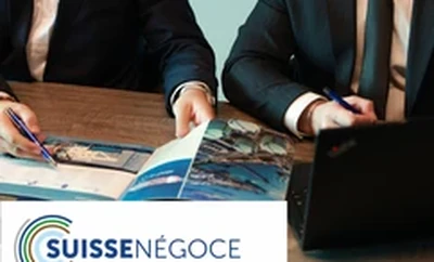 A meeting table with individuals reviewing a printed brochure, laptops open, and the SUISSENÉGOCE logo visible on a document.