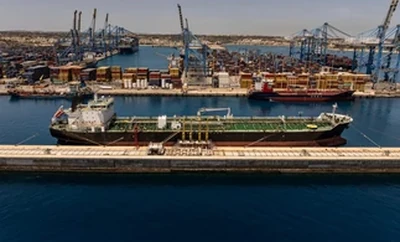 Aerial view of a busy industrial port with multiple cargo ships docked along the waterfront and cranes positioned throughout the terminal.