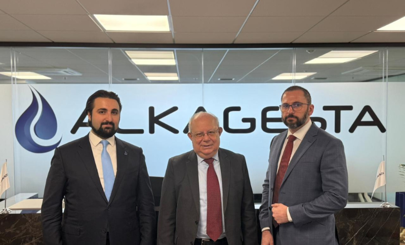 Three individuals standing in an office environment in front of a wall with the Alkagesta logo.