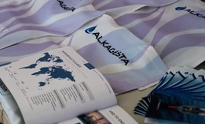 Alkagesta‑branded brochures and documents laid out on a table, including an open booklet showing a world map and company information.