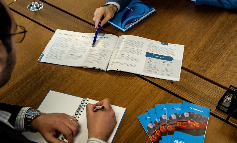 People sitting at a table reviewing an open booklet, taking notes, and organizing brochures during a meeting.