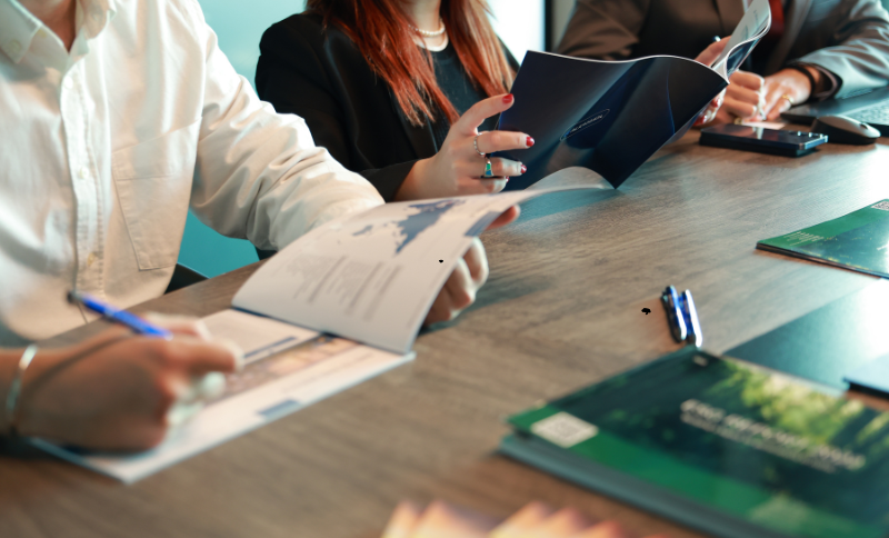 People sitting at a table reviewing documents and writing notes during a meeting.