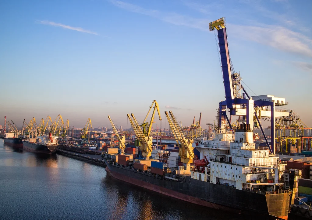 A cargo port with cranes, containers, and docked ships along the waterfront.