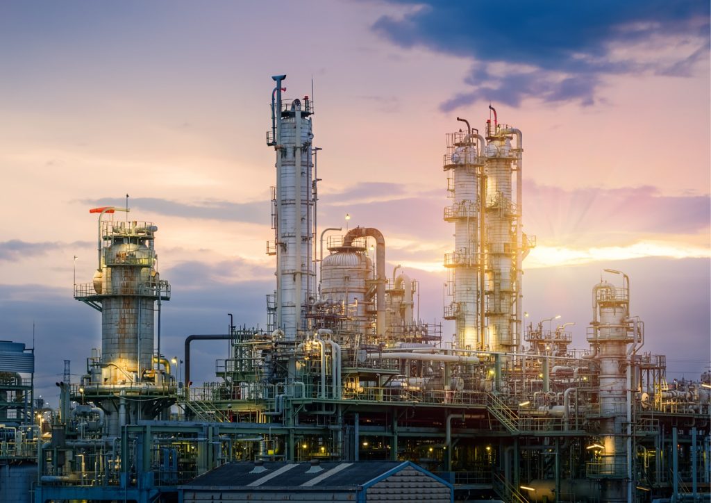 Large industrial refinery with metal towers, pipelines, and processing structures under a sunset sky.