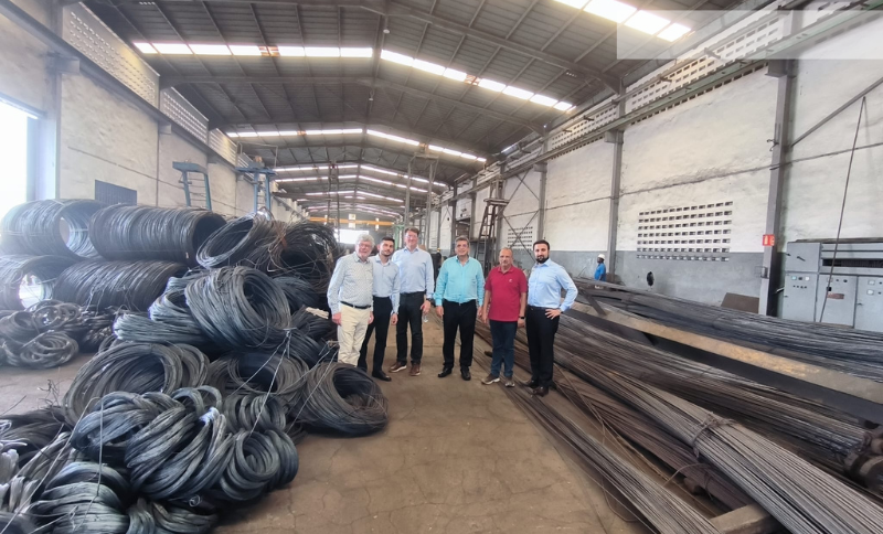 “Individuals standing inside an industrial warehouse inspecting stacked metal rods and large wire coils during Alkagesta’s West Africa site visit.