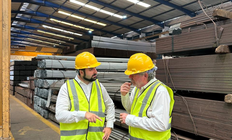 Two individuals in safety vests and helmets discussing stacked metal beams inside an industrial storage facility during Alkagesta’s West Africa site visit.