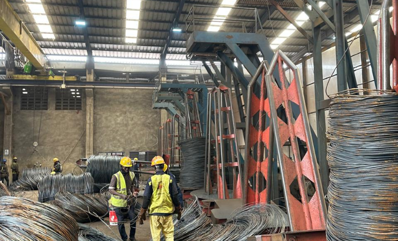 Workers in safety gear handling large steel wire coils inside an industrial manufacturing facility during Alkagesta’s West Africa site visit.