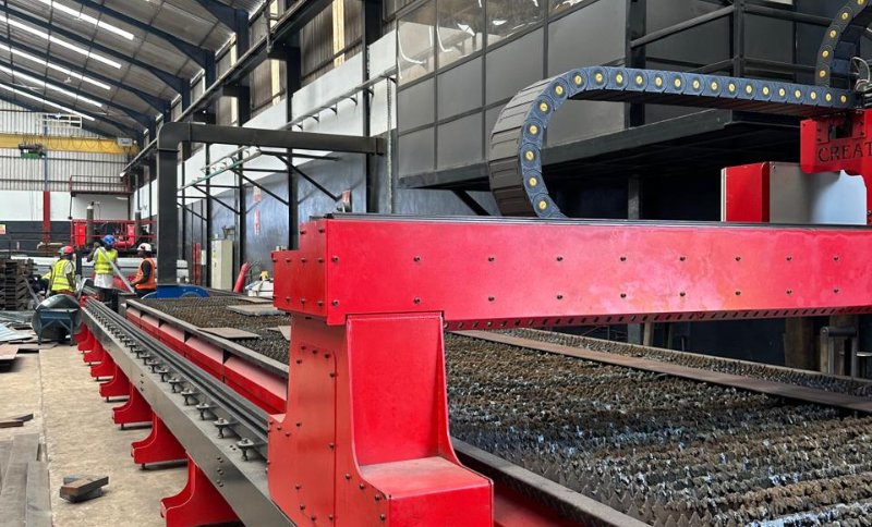 Industrial metal cutting machinery in operation inside a manufacturing facility during Alkagesta site visit