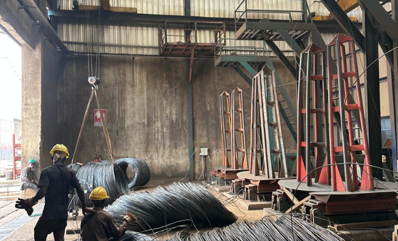 workers handling steel wire coils inside industrial facility using lifting equipment