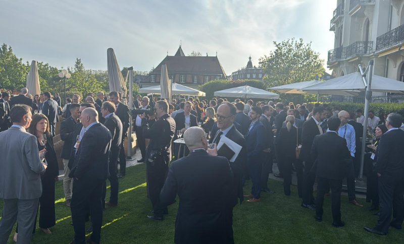 Attendees gathered outdoors during a networking reception at the FT Commodities Global Summit, standing on a lawn area with umbrellas and historic buildings visible in the background.