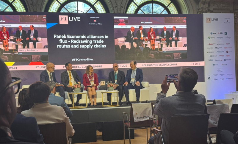 A panel discussion taking place on the main stage of the FT Commodities Global Summit, with several speakers seated on stage and presentation screens visible behind them displaying session information.