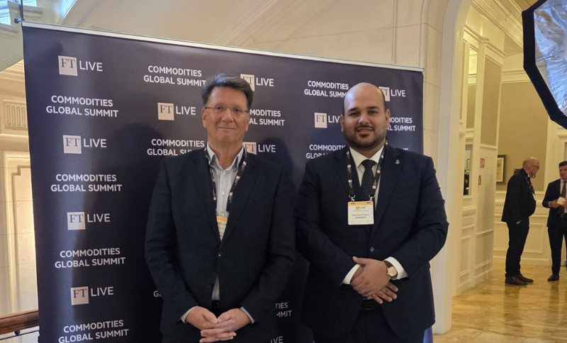 Two conference participants standing in front of an FT Commodities Global Summit step‑and‑repeat backdrop, with event branding and logos visible behind them inside the conference venue.