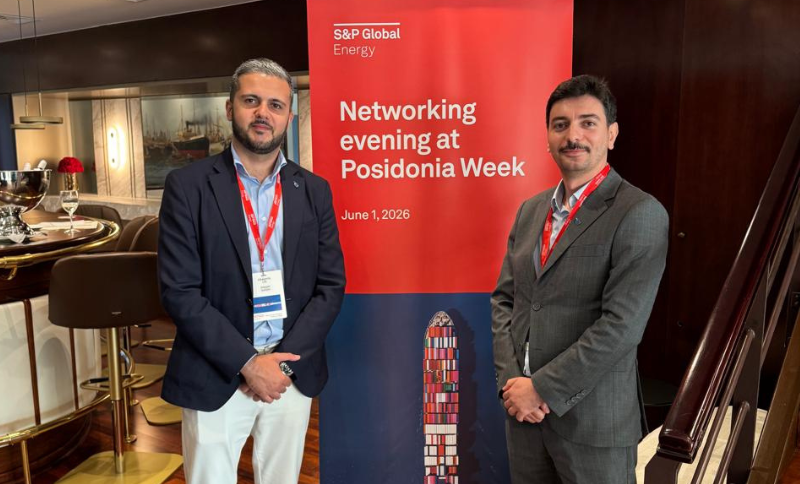 Two men in business attire stand next to a red S&P Global Energy banner that reads Networking evening at Posidonia Week, 1 June 2026, in a modern indoor setting.