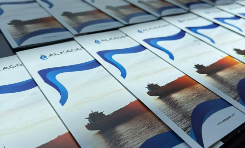 Several brochures with a blue wave design and a ship silhouette on the cover are arranged in neat rows. The brochures feature the ALKAGES logo and website address.
