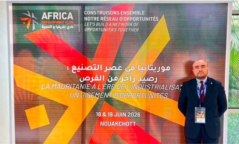 A man in a suit stands next to a colourful backdrop with geometric designs at the Africa Development Club event in Nouakchott, dated 18-19 June 2026. The banner displays text in French, Arabic, and English.