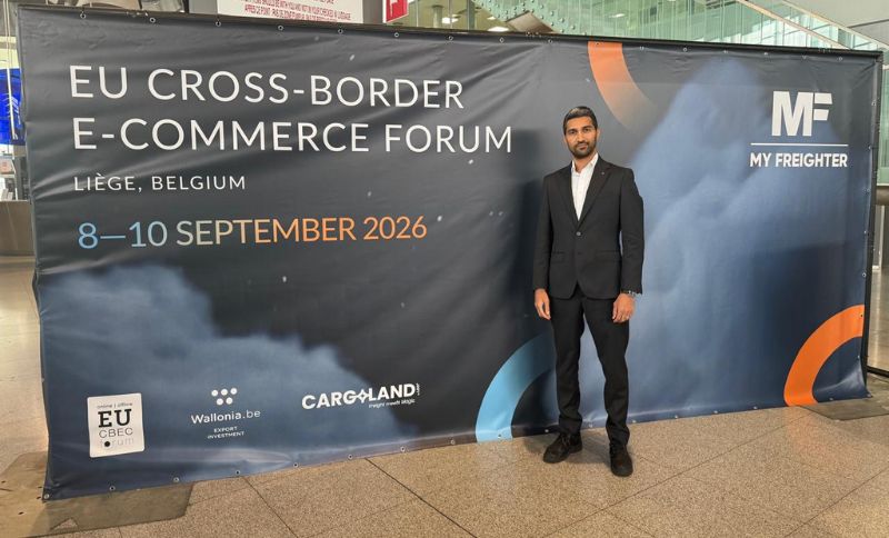 A man in a suit stands beside a large banner for the EU Cross-Border E-Commerce Forum, held in Liège, Belgium, from 8–10 September 2026. The banner includes event sponsors and the My Freighter logo.