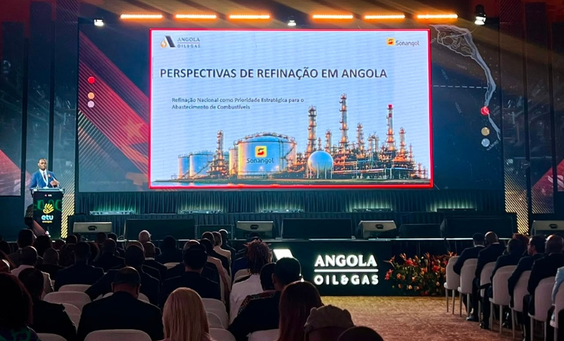 A speaker presents to an audience at the Angola Oil & Gas conference. The screen displays slides about oil refining perspectives in Angola, featuring refinery imagery and company logos.