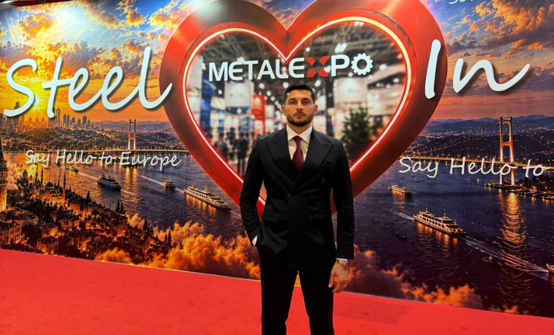 A man in a suit stands on a red carpet in front of a METAL EXPO backdrop featuring a cityscape, heart design, and phrases Steel In and Say Hello to Europe.
