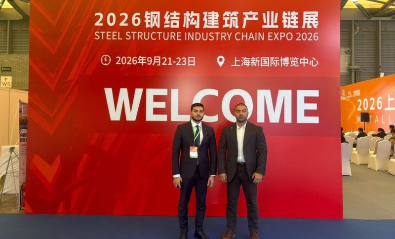 Two men in suits stand in front of a red expo backdrop with 2026 Steel Structure Industry Chain Expo and WELCOME written in English and Chinese at the Shanghai New International Expo Centre.