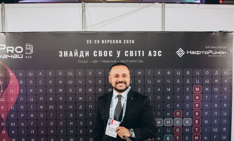 A man in a suit stands smiling in front of a backdrop with Cyrillic text and event details, including the dates 22-23 September 2026, at a business conference or expo.