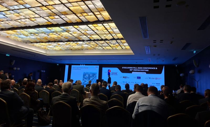 A speaker addresses an audience seated in a dark conference hall facing a large screen displaying the title SteelOrbis Autumn 2026 Conference & 95th IREPAS Meeting.