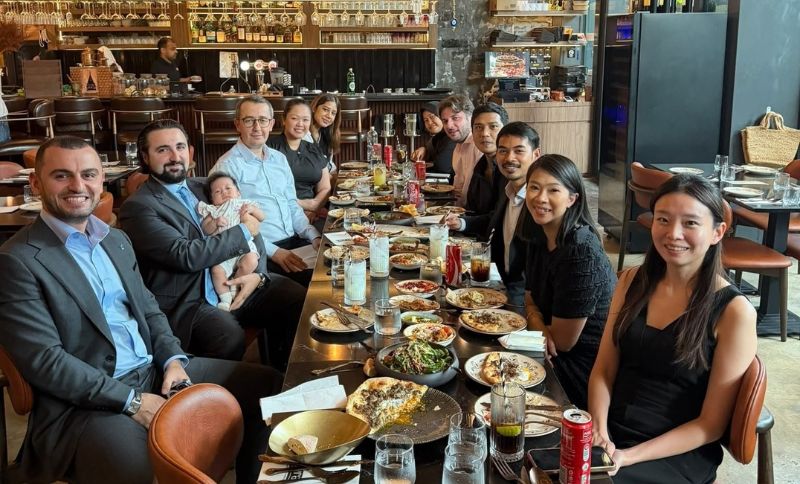 A group of people sitting around a long restaurant table filled with shared dishes, with one man holding a baby.