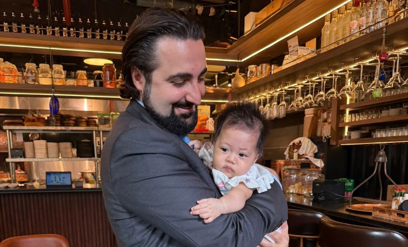 A man in a suit jacket holding a baby in a restaurant.