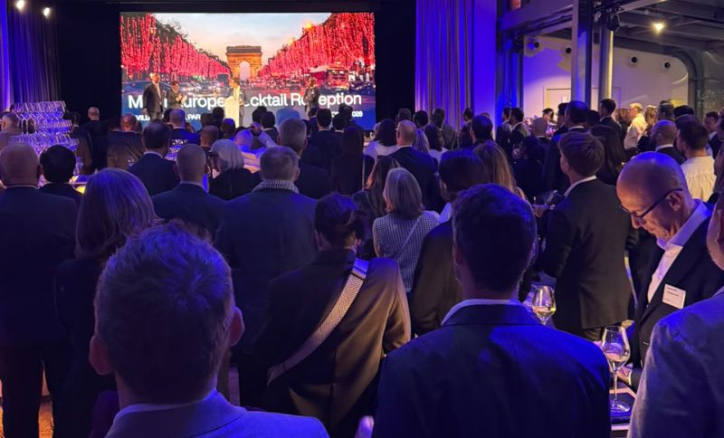 A large crowd stands in a darkened event hall facing a screen displaying an image of the Arc de Triomphe and text reading MIPIM Europe Cocktail Reception.