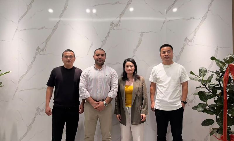 Four people standing in a row in front of a white wall with grey veining.