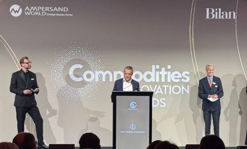 A man speaks at a lectern at the Commodities Innovation Awards, flanked by two men standing on stage.