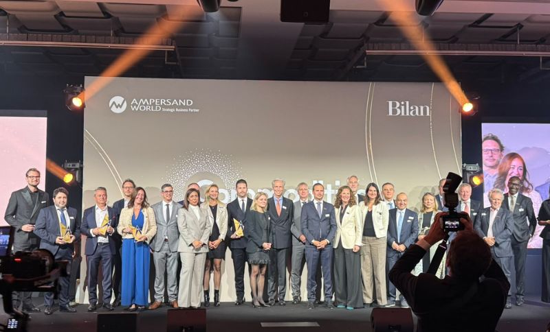 A large group of people in business attire standing on a stage at an awards ceremony, with company logos displayed on the backdrop.