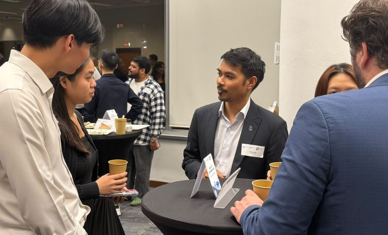 A group of people standing around high-top tables at an indoor networking event.