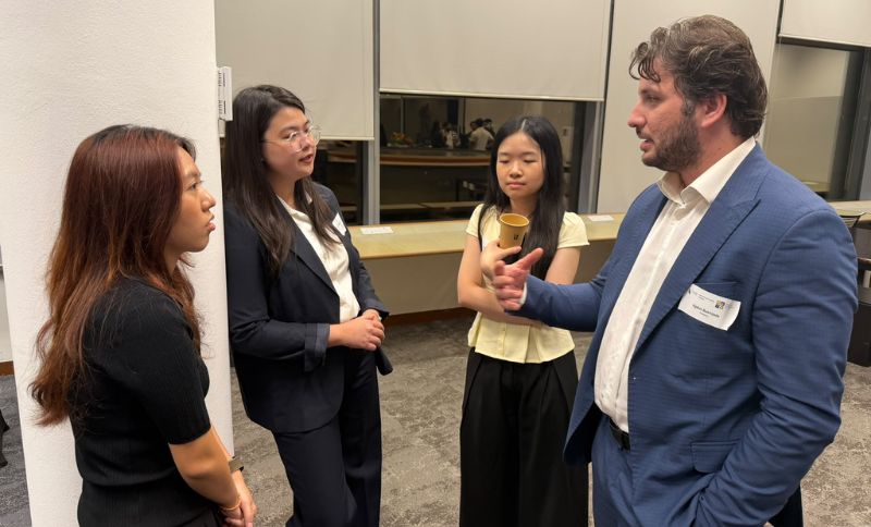 A man in a suit speaks to three women in a professional office setting.