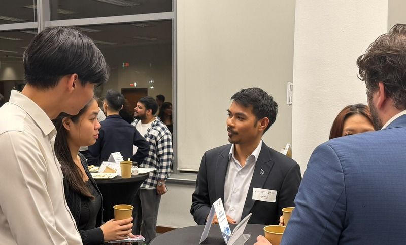A group of people talking and holding paper cups at an indoor networking event.