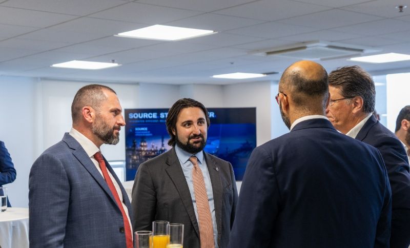 Four men in business suits stand together in an office, engaged in conversation.