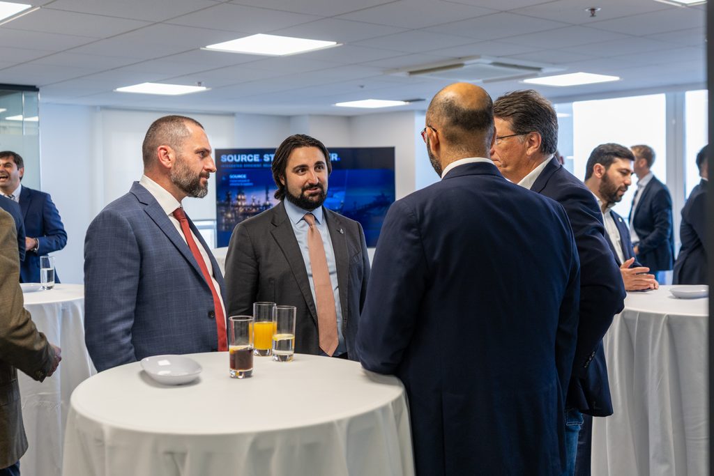 A group of men in business attire networking around high-top tables at an office event.