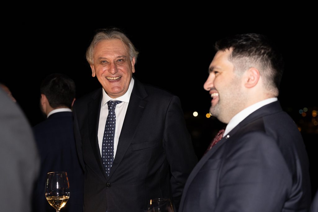 Two men in suits smiling and talking at an evening event.