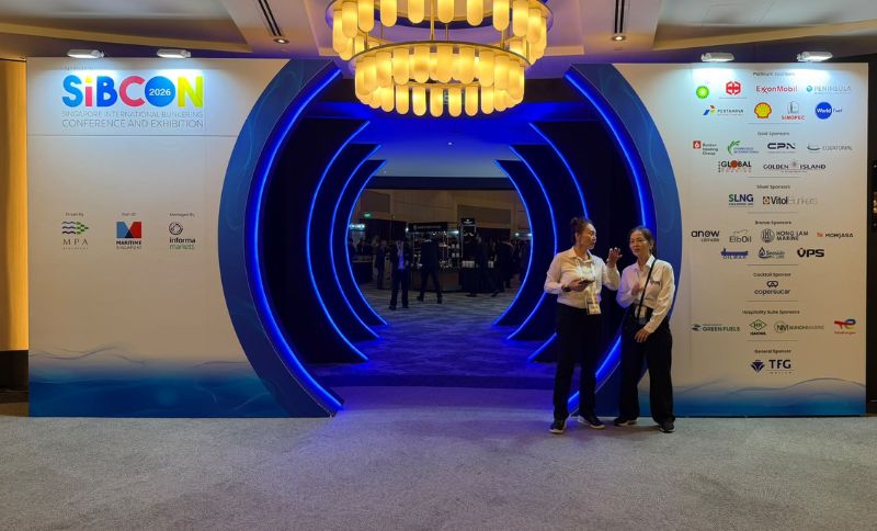Two women stand in front of a SIBCON 2026 conference entrance featuring a large, blue-lit circular tunnel and walls displaying event logos and sponsors.