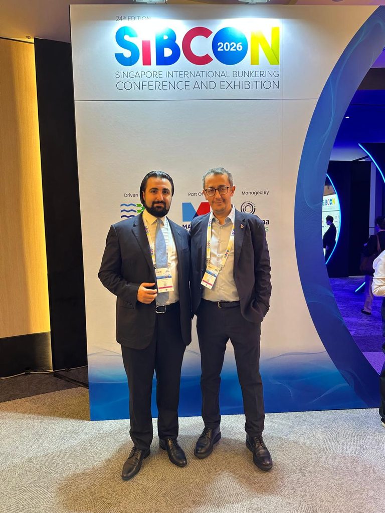 Two men in suits and conference badges stand in front of a SIBCON 2026 conference backdrop.