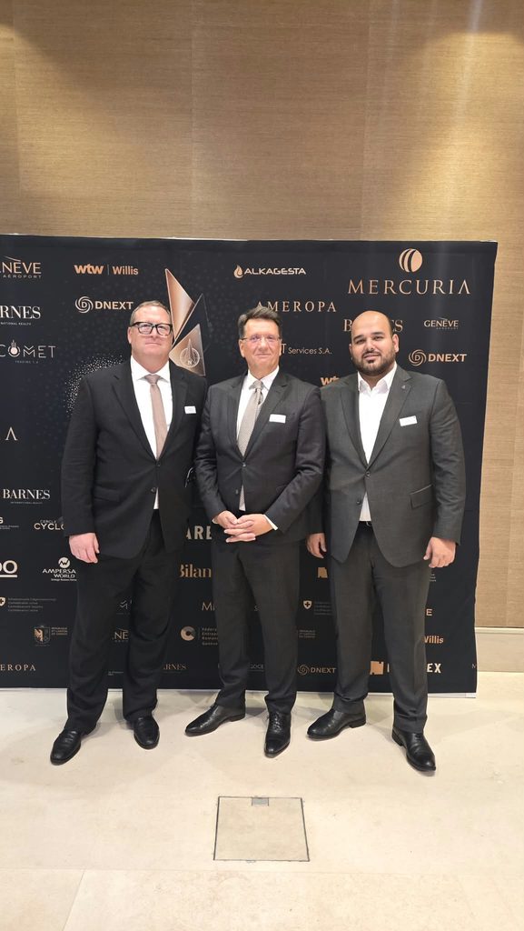 Three men in business suits stand side-by-side in front of a step-and-repeat banner featuring various corporate logos.